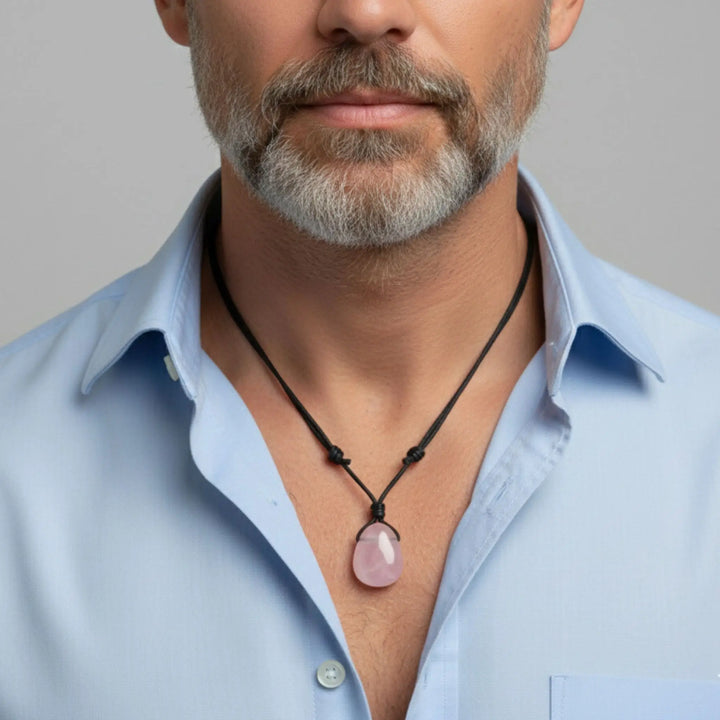 Man wearing a light blue shirt with a rose quartz pendant necklace against a neutral background