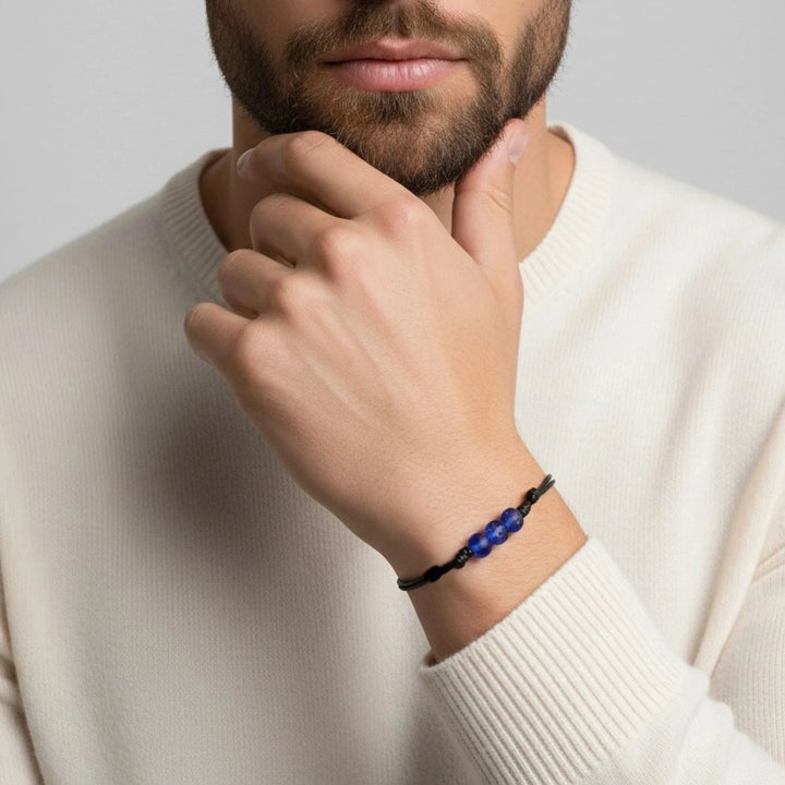 Man wearing a white sweater with a blue beaded bracelet on his wrist, against a plain background.