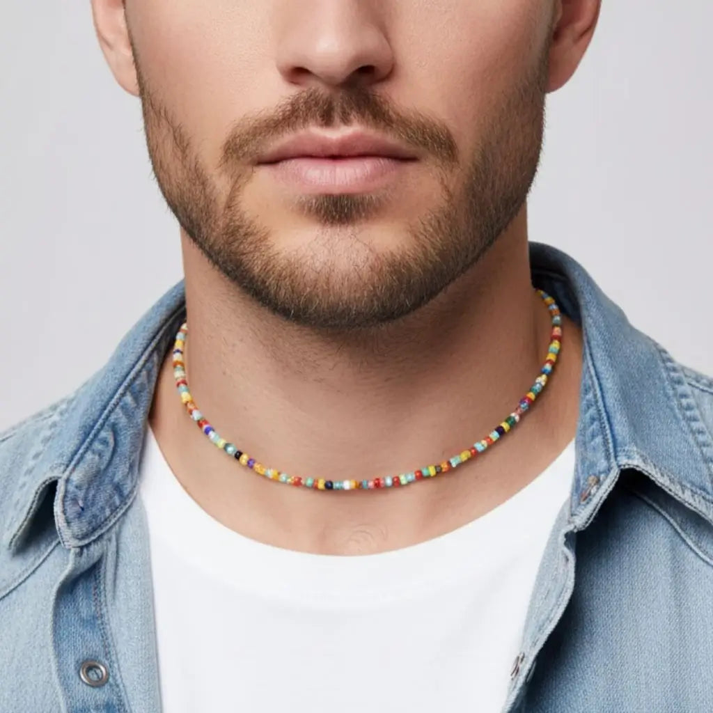 Man wearing a colorful beaded necklace with a denim jacket and white shirt on a light gray background