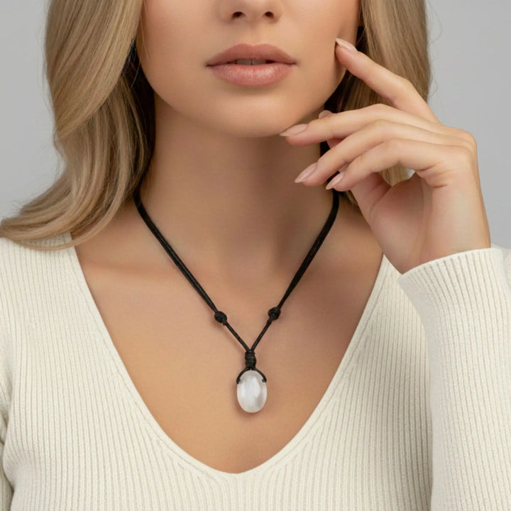 Woman wearing a necklace with a white selenite pendant against a neutral background