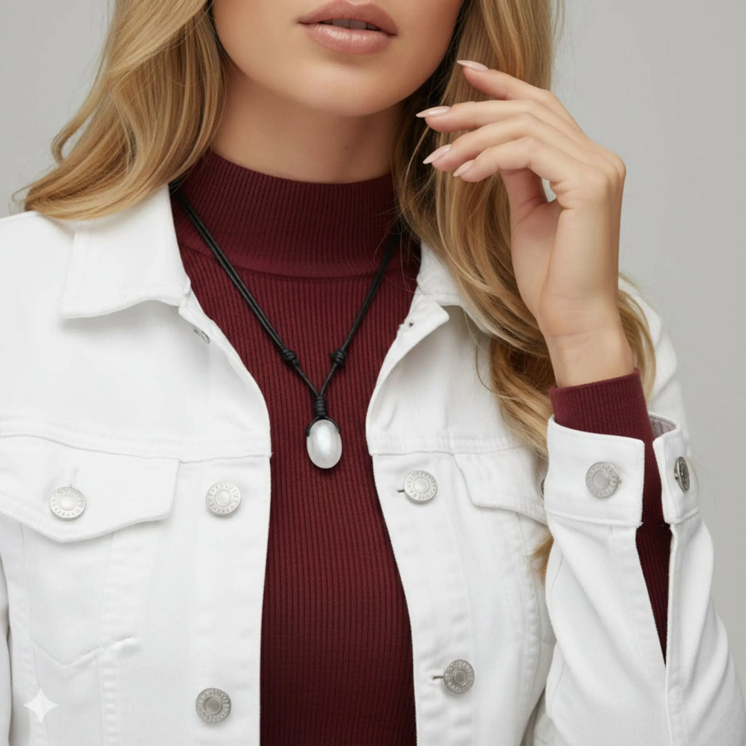 Person wearing a white jacket over a burgundy turtleneck with a selenite necklace.