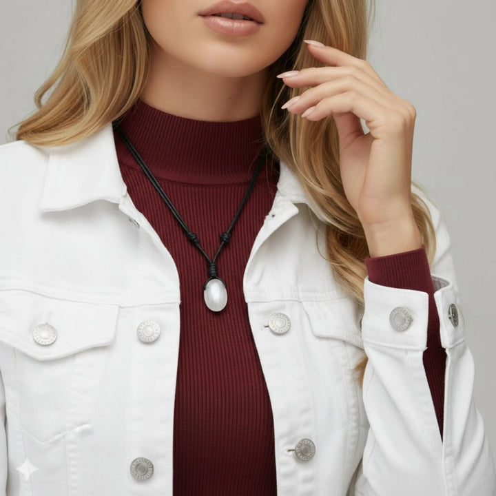 Person wearing a white jacket over a burgundy turtleneck with a selenite necklace.