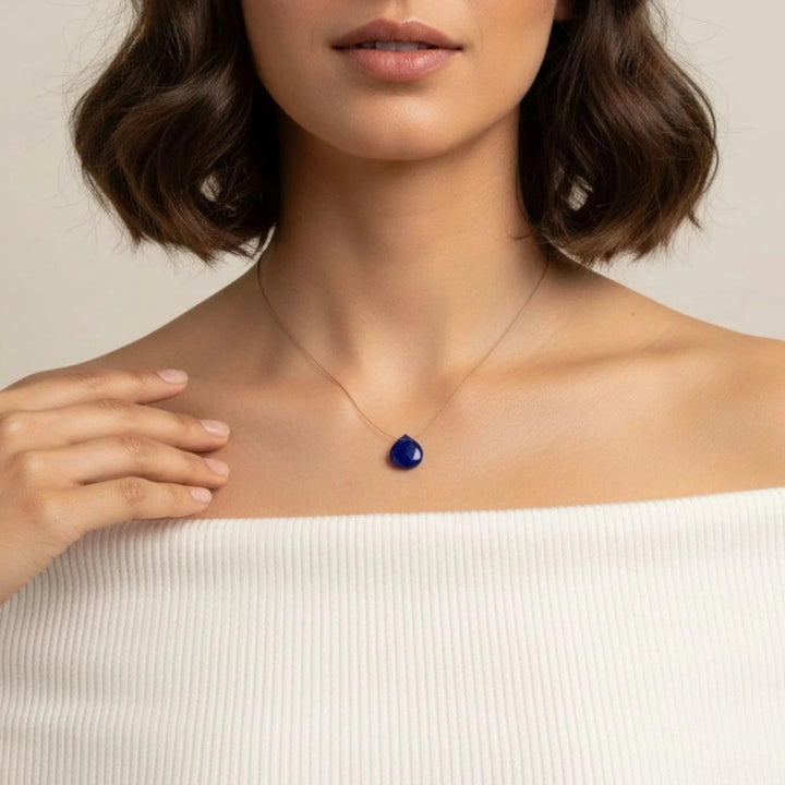 Woman wearing a necklace with a lapis lazuli pendant against a neutral background