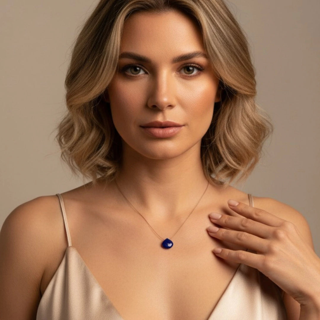 Woman wearing a necklace with a  lapis lazuli  pendant against a neutral background