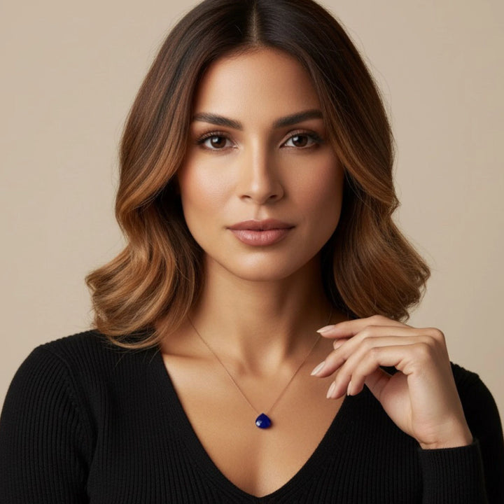 Woman wearing a black top and a necklace with a  lapis lazuli  pendant against a beige background