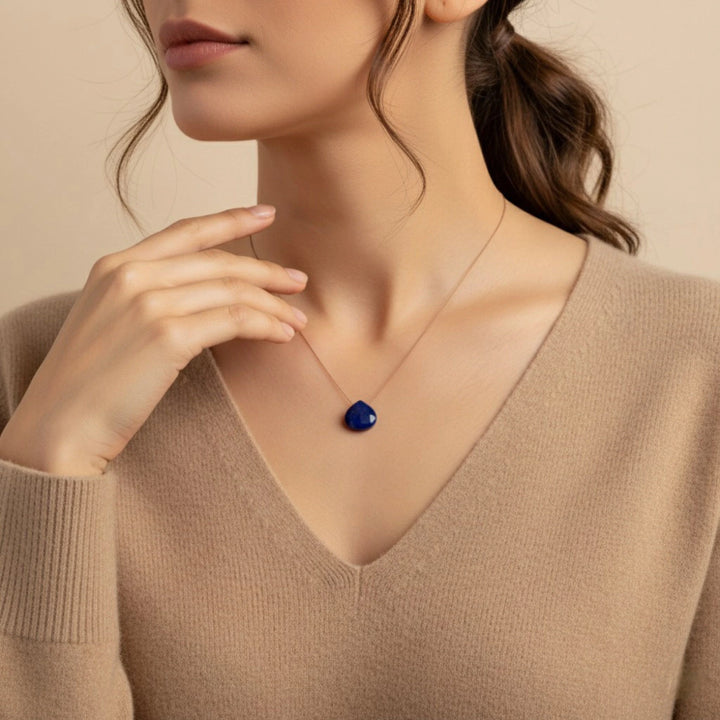 Woman wearing a necklace with a lapis lazuli heart pendant against a beige background