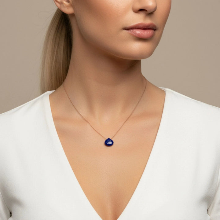 Woman wearing a necklace with a lapis lazuli pendant against a neutral background