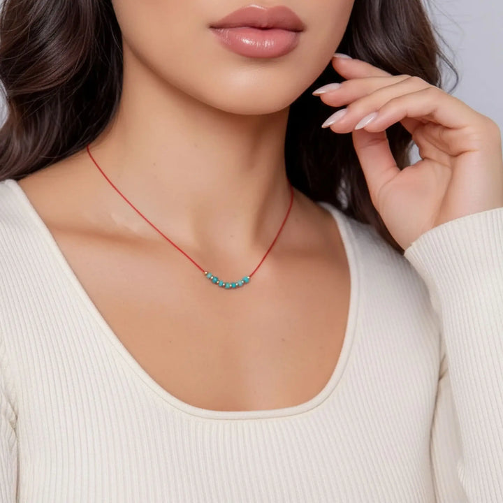 Woman wearing a red necklace with a turquoise pendant against a neutral background