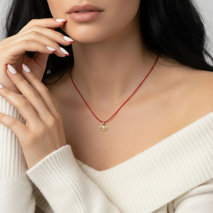 Woman wearing a red gold evil eye necklace with a gold pendant, close-up of neck and hand.