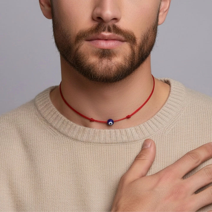 Man wearing a red Woman with styled blonde hair wearing a beige top and black evil eye necklace against a neutral background. necklace with a blue eye pendant against a neutral background