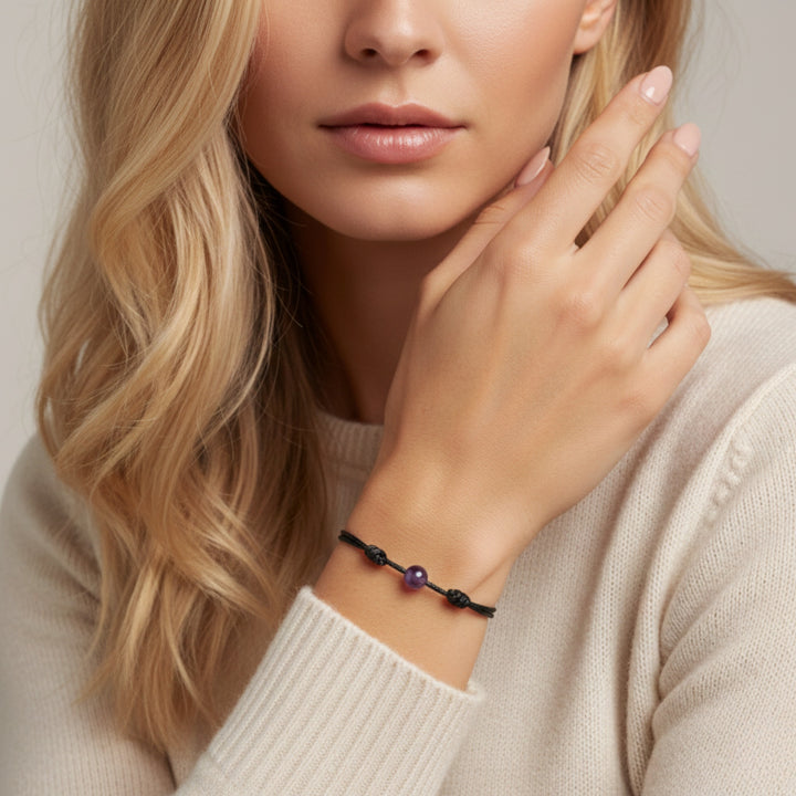Woman wearing smooth amethyst single bead bracelet on black waxed nylon cord.

