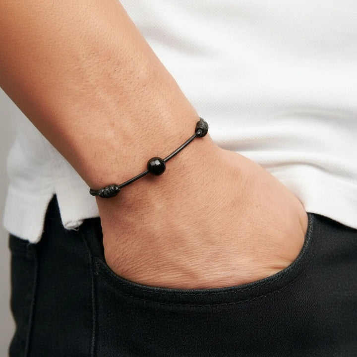 Man wearing smooth black tourmaline bead bracelet on black waxed nylon cord with hand in pocket.