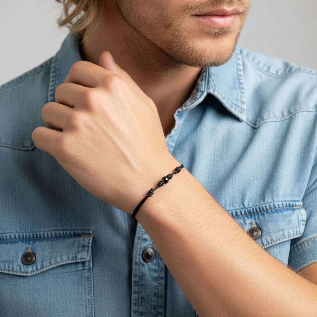 Man wearing smooth black tourmaline round bead bracelet on black nylon cord.