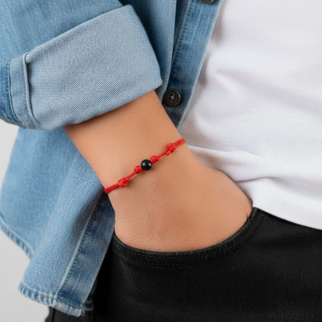 Smooth black tourmaline round bead bracelet on red nylon cord worn on wrist.