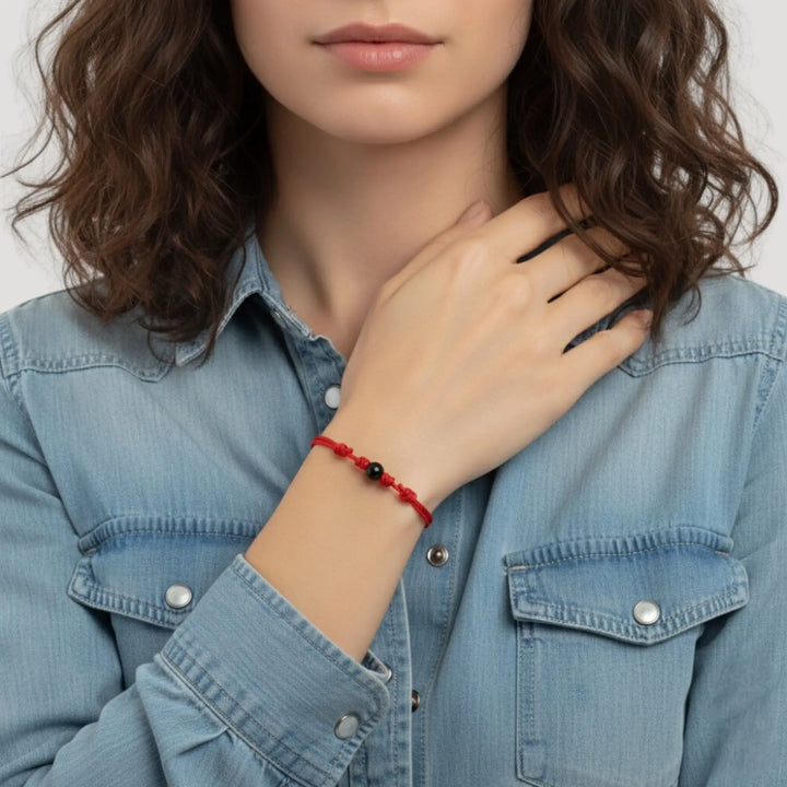 Woman wearing smooth black tourmaline round bead bracelet on red nylon cord.