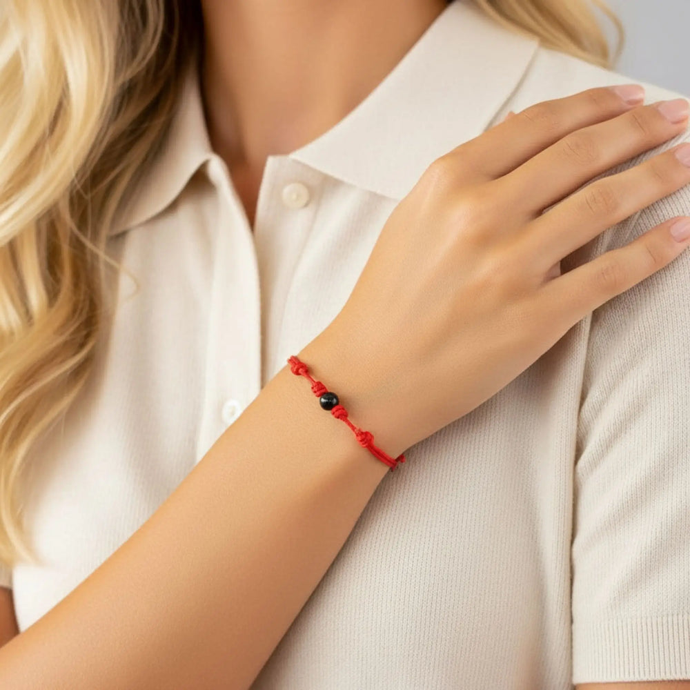Woman wearing smooth black tourmaline round bead bracelet on red nylon cord.