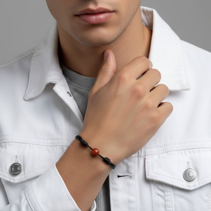 Man wearing smooth carnelian single bead bracelet on black waxed nylon cord.

