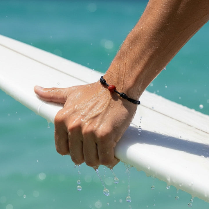 Man wearing smooth carnelian single bead bracelet on black waxed nylon cord.
