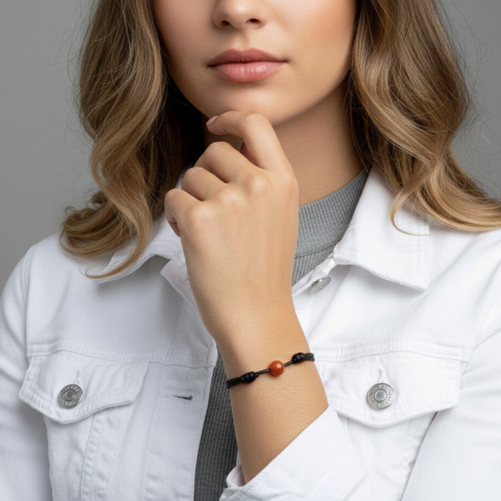 Woman wearing smooth carnelian single bead bracelet on black waxed nylon cord.
