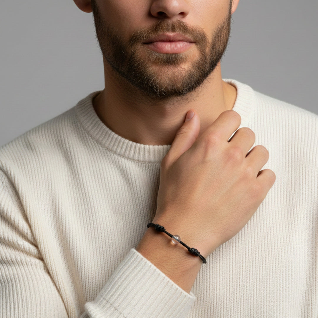 Man wearing smooth clear quartz single bead bracelet on black waxed nylon cord.

