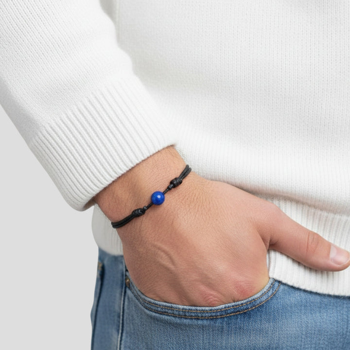 Man wearing smooth lapis lazuli single bead bracelet on black waxed nylon cord.

