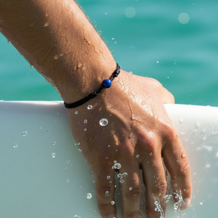 Man wearing smooth lapis lazuli single bead bracelet on black waxed nylon cord.
