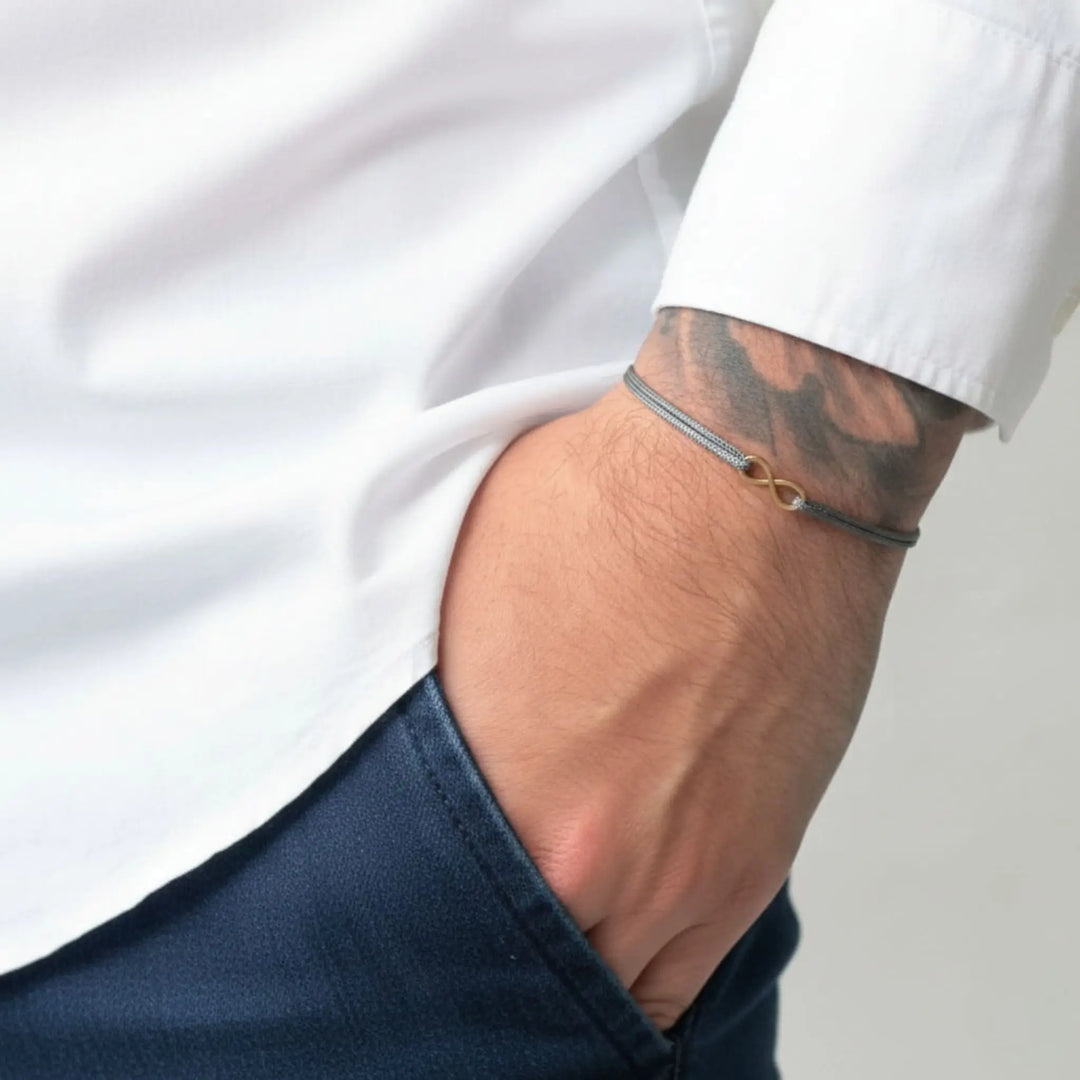 Close-up of a person wearing a gold infinity bracelet on a plain background