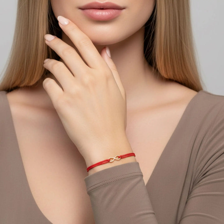 Woman wearing a red bracelet with a gold infinity on a neutral background