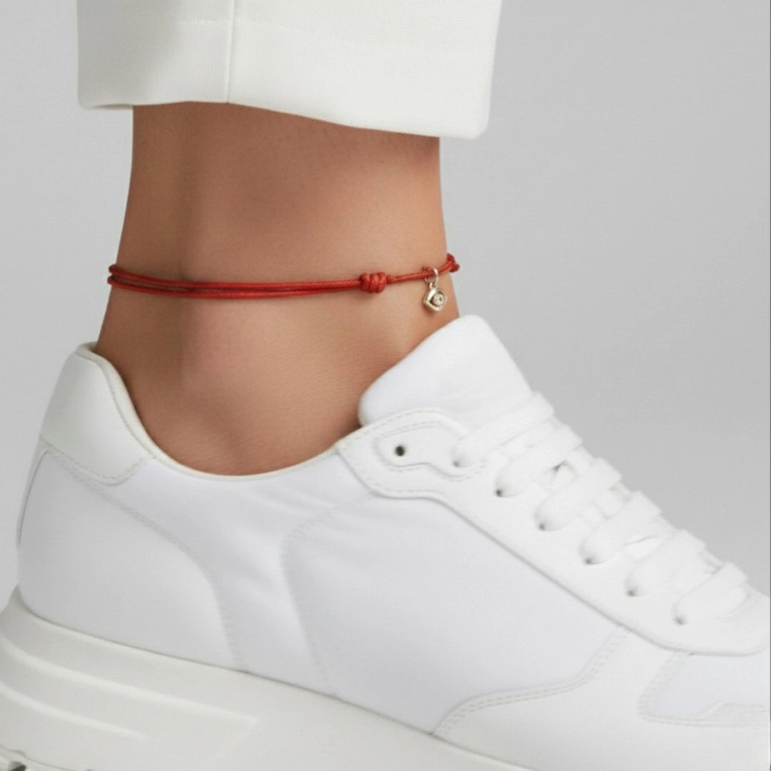 Red anklet on a person's ankle with a white sneaker