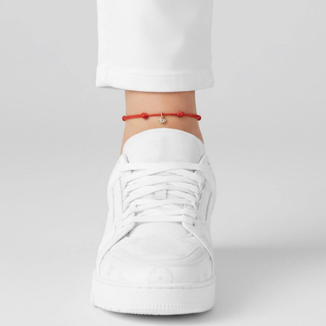 White sneaker worn with a red anklet on a plain background