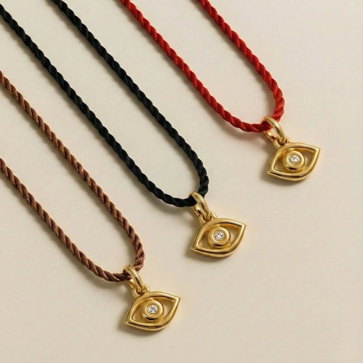 Three necklaces with gold eye-shaped pendants on red, black, and brown cords.