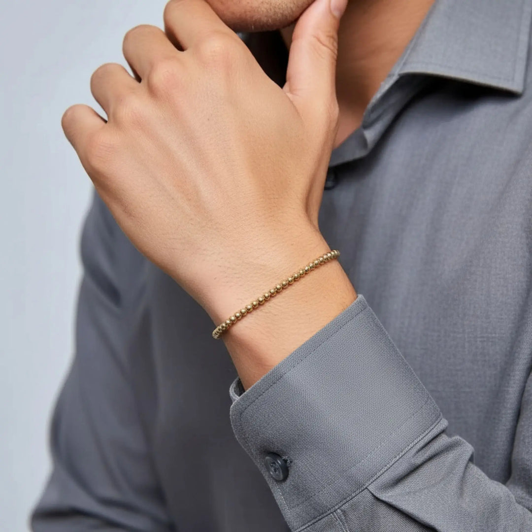 Person wearing a gold bracelet on a plain background