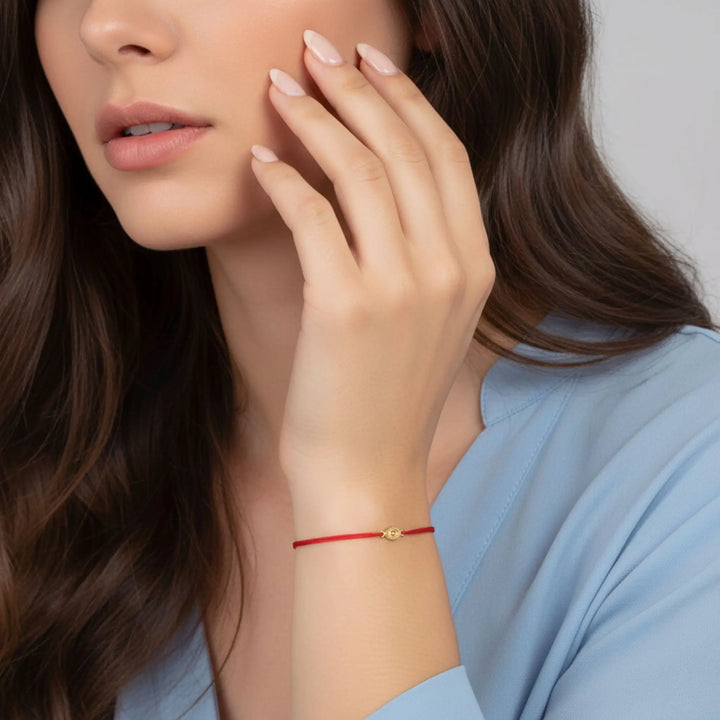 Woman wearing a gold evil eye red bracelet on her wrist, with a neutral background