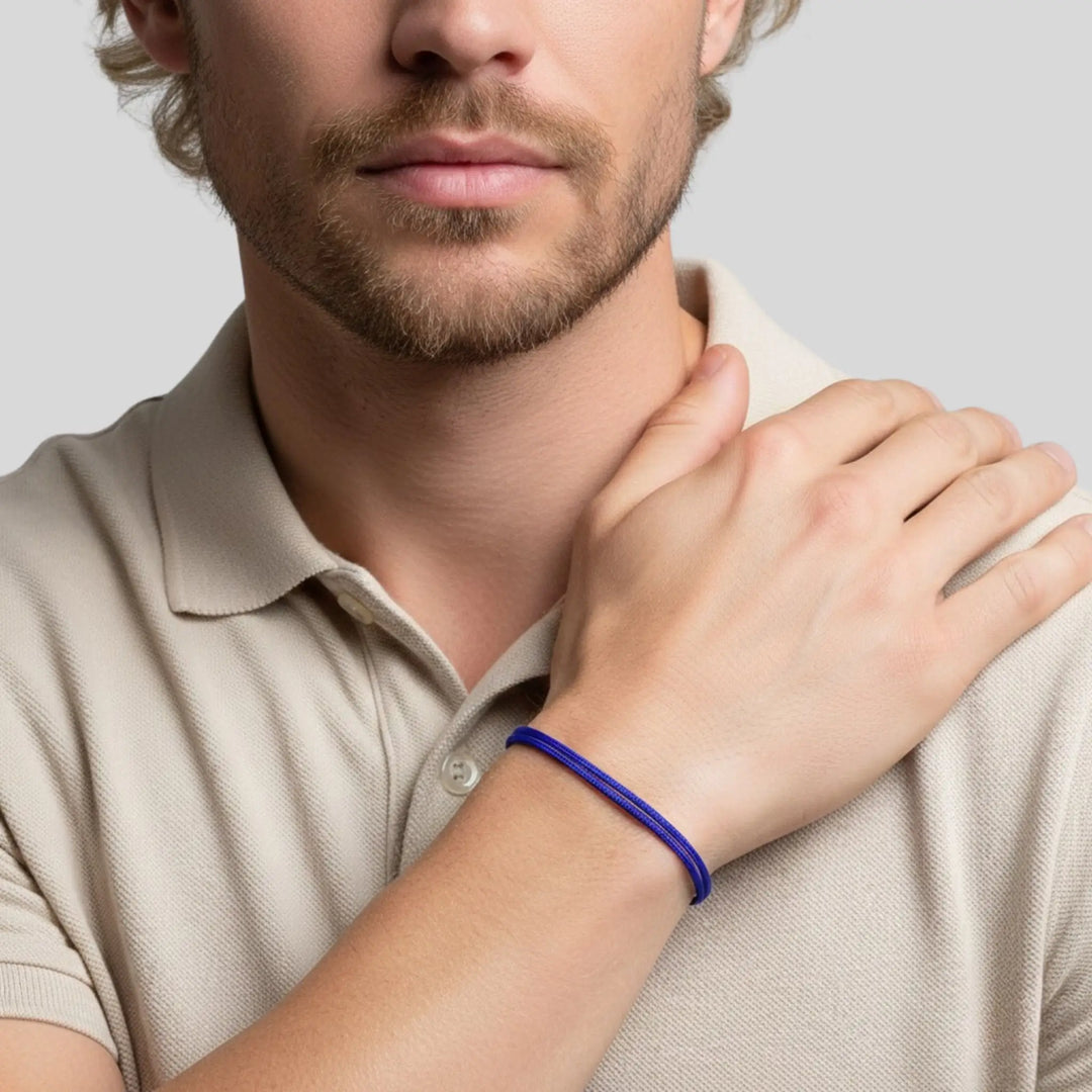 Man wearing a beige polo shirt with a blue bracelet on his wrist, against a light gray background