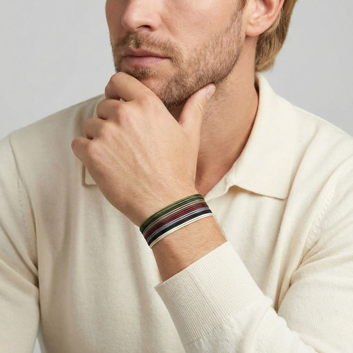 Man wearing a beige sweater with a colorful bracelet on his wrist against a light gray background