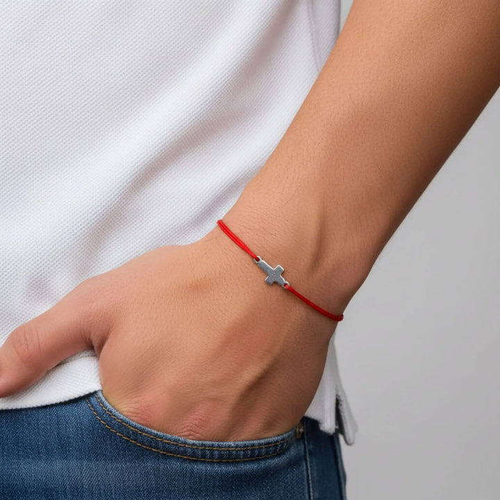 Person wearing a red bracelet with a silver cross charm on a neutral background