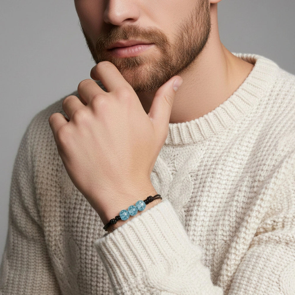 Man wearing a beige sweater with a glass bracelet on his wrist, against a neutral background