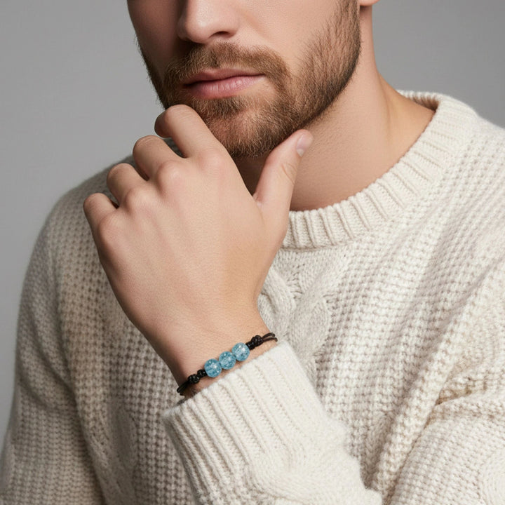Man wearing a beige sweater with a glass bracelet on his wrist, against a neutral background