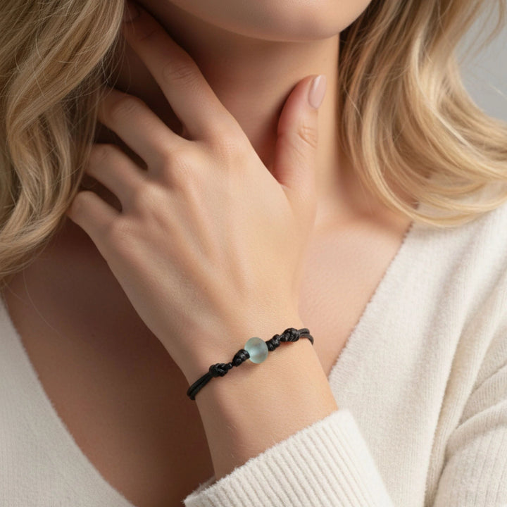Close-up of a person wearing a black bracelet with glass bead on a neutral background