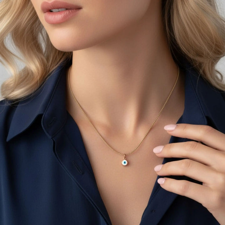 Close-up of a person wearing a gold evil eye necklace with a small pendant.