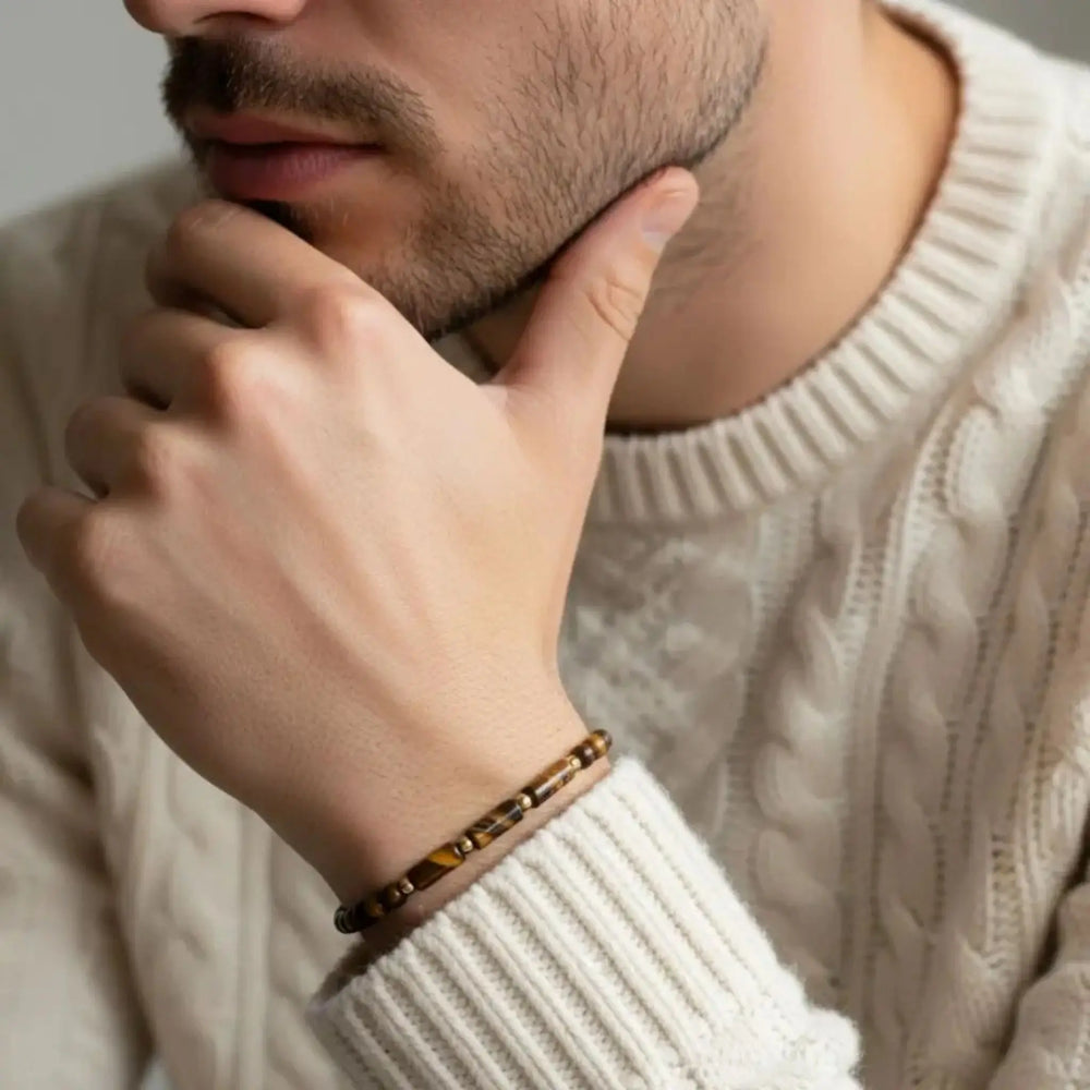 Close-up of a person wearing a white sweater and a tiger eye bracelet, with a neutral background.
