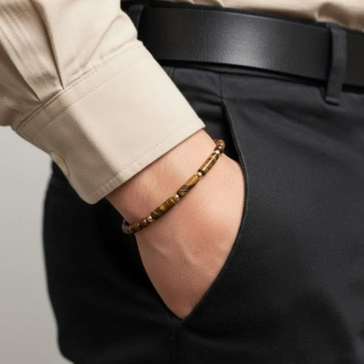 Men’s Tiger’s Eye bracelet with 14K gold accents, worn with beige shirt and black trousers.