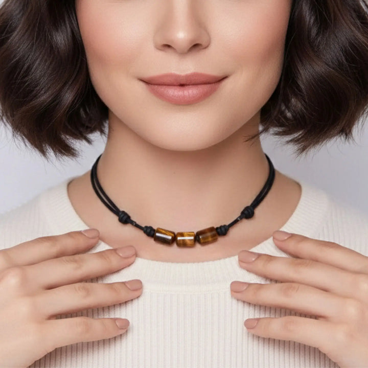 Woman wearing a necklace with tigers eye brown beads, holding it with both hands against a neutral background