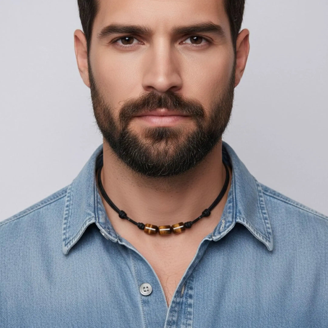 Man wearing a blue denim shirt and a tigers eye necklace with a gray background