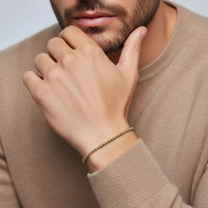 Close-up of a person wearing a gold bracelet on a neutral background