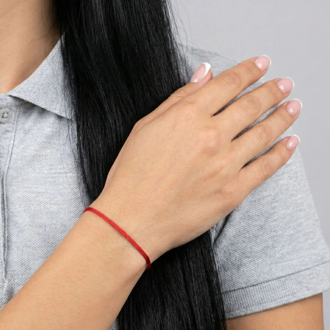 Person wearing a red bracelet on a neutral background