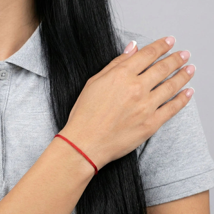 Person wearing a red bracelet on a neutral background