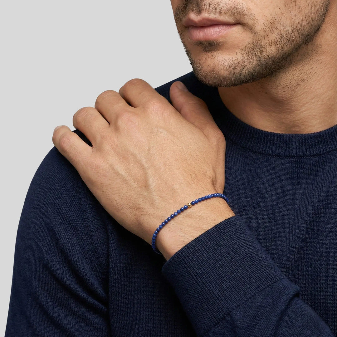 Man wearing a navy blue sweater with a close-up of his hand and lapis lazuli bracelet on a light gray background