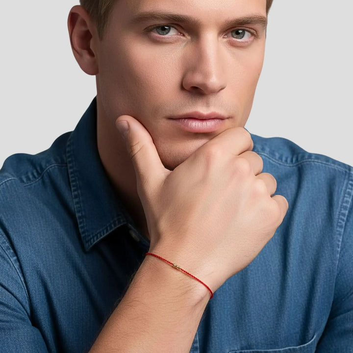 Man wearing a blue shirt with a red bracelet on his wrist, posing with hand on chin.