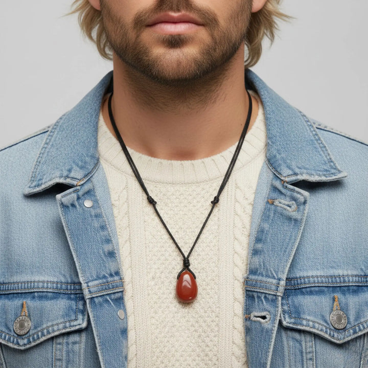 Man wearing a denim jacket and white sweater with a jasper necklace featuring a red pendant.